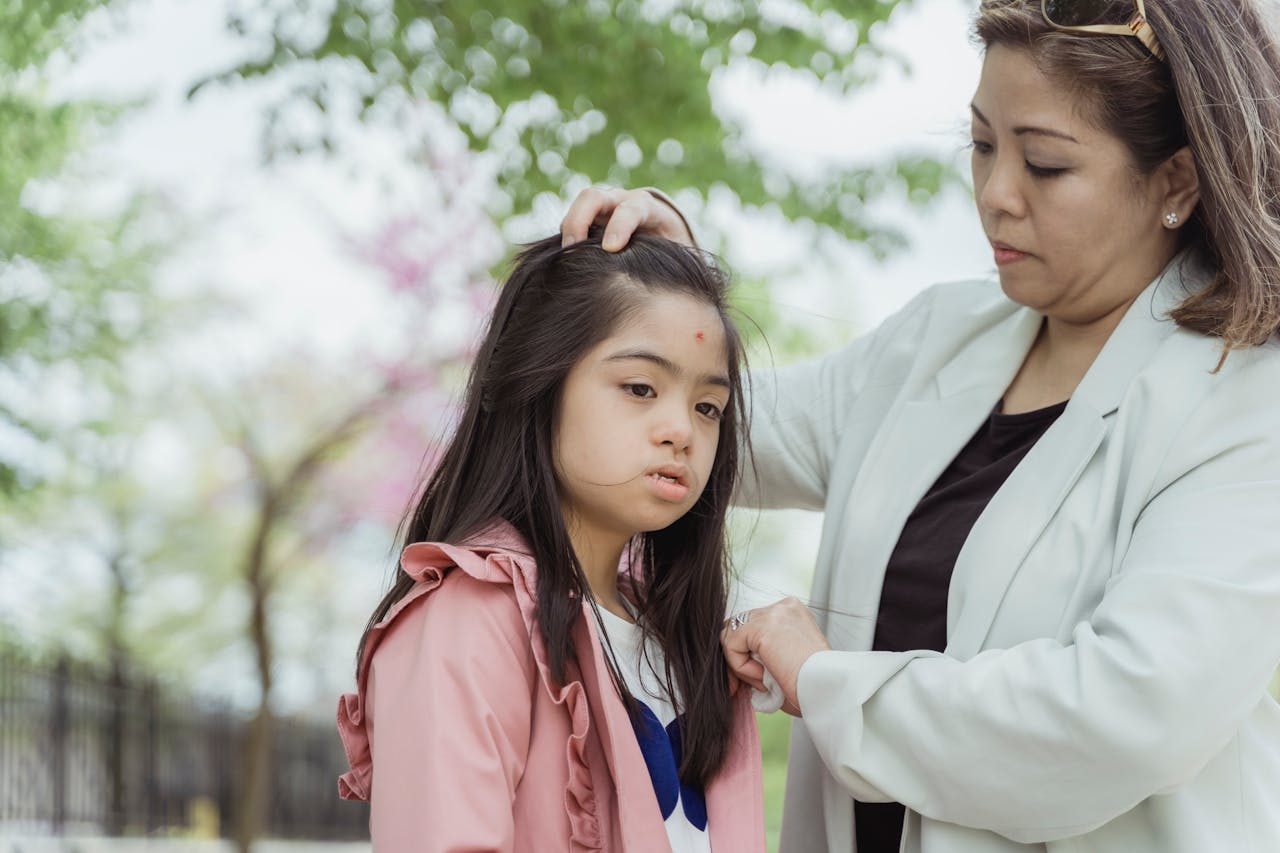 Mother gently helps her daughter adjust her hair during outdoor quality time.